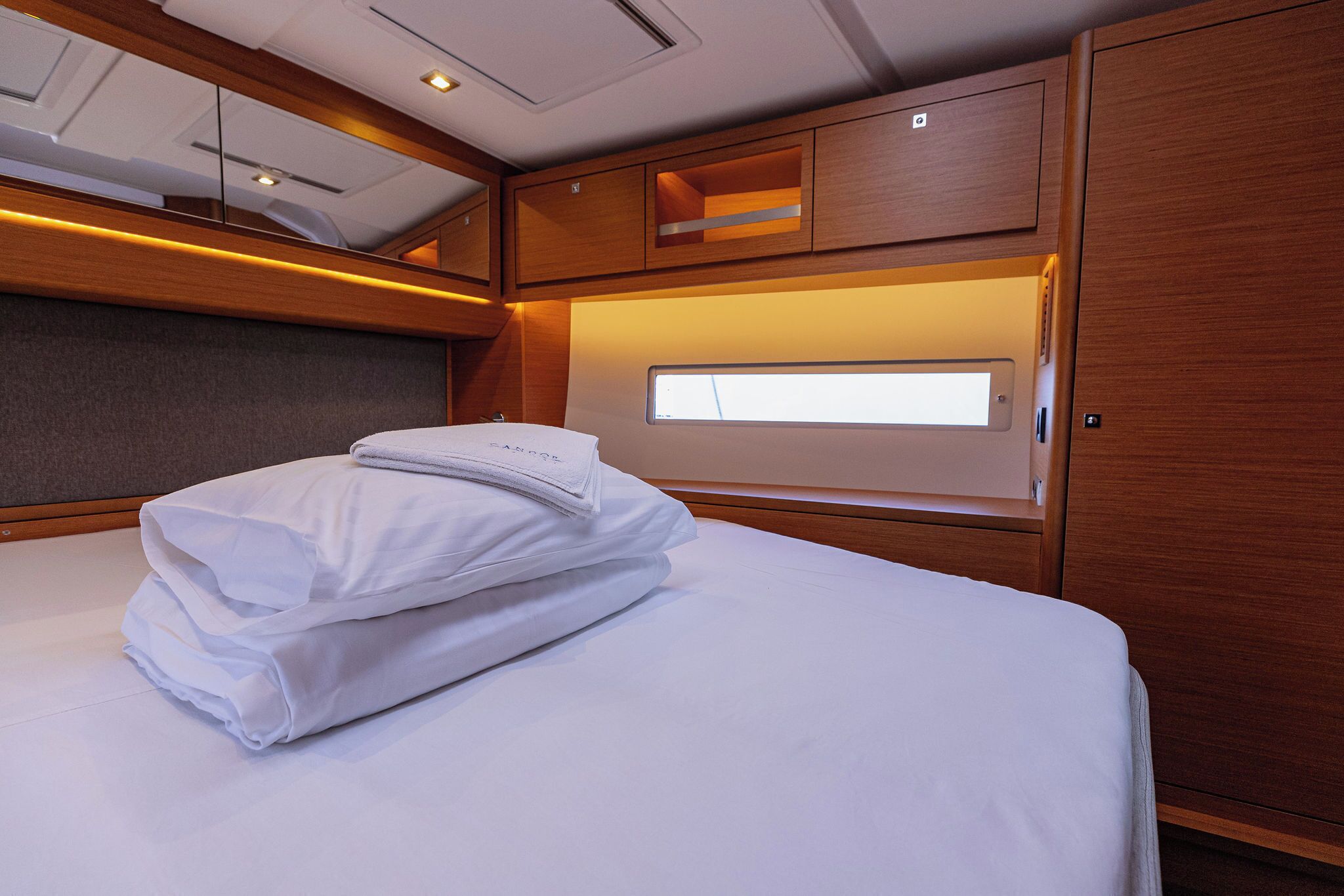 Una cama bien hecha con sábanas blancas dobladas, un cabecero de madera y una ventana con vistas.