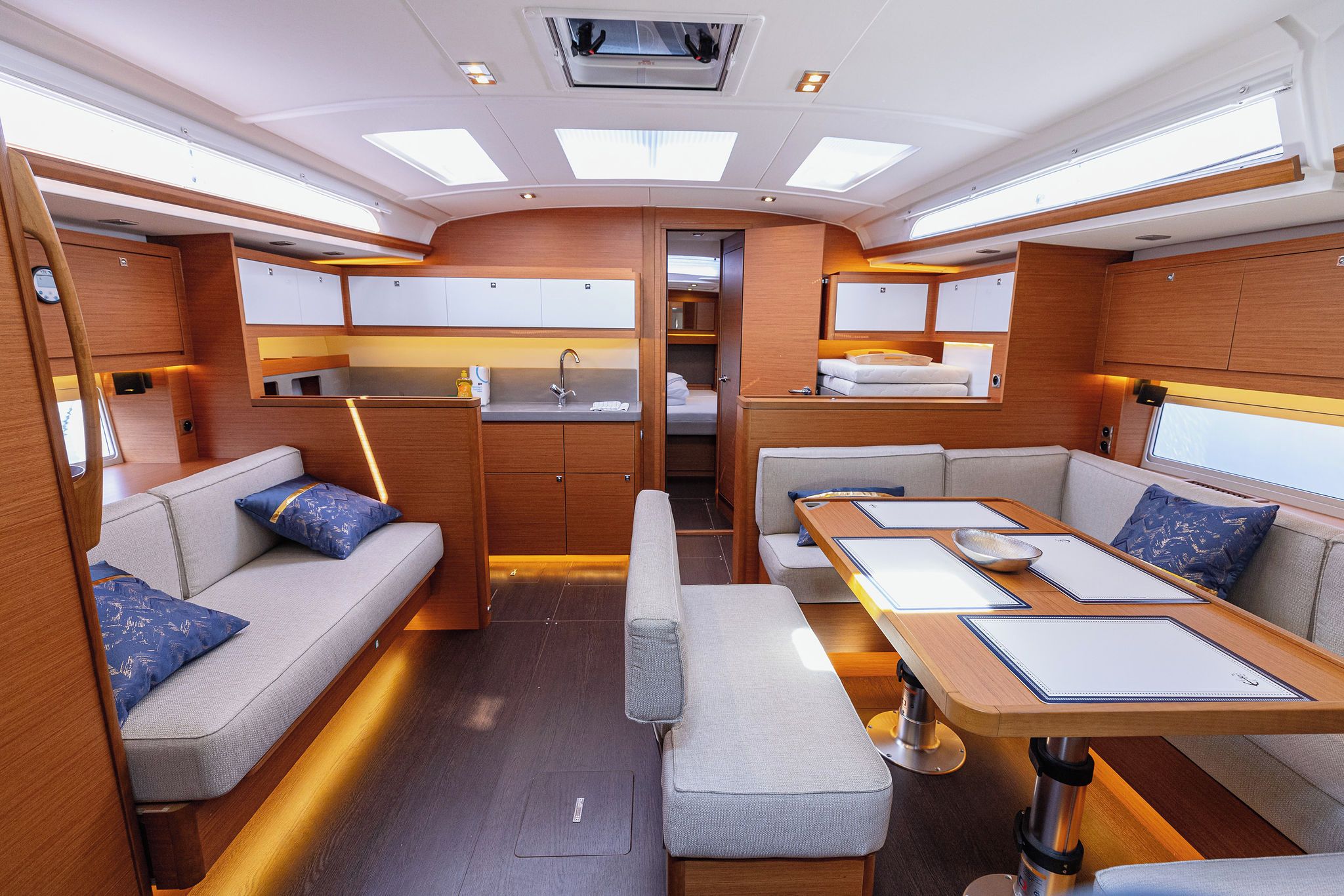 A compact interior with a sofa, a dining table, a bench, and a kitchenette.