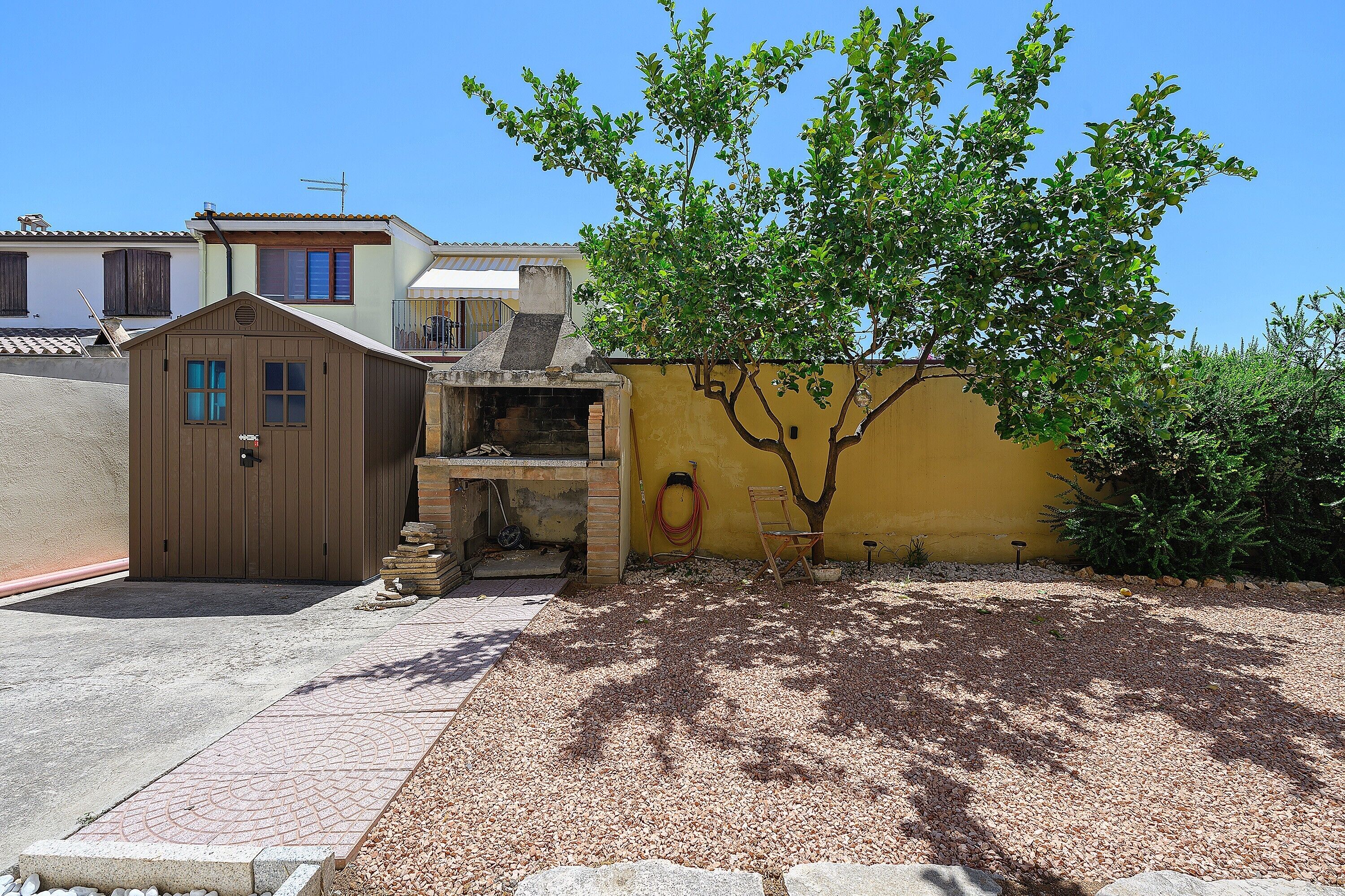 A residential area with a small wooden shed, a yellow wall, and a tree providing shade.