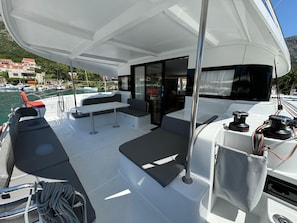 A boat deck with seating, a table, and a view of the marina. - Dubrovnik Delight: A Sun-Kissed Sailing Experience (Komolac)