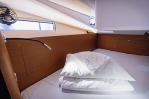 A neatly made bed with white linens, a wooden headboard, and a small window with a view. - Sun-Kissed Sailing Adventure in Split, Croatia (Kaštel Gomilica)