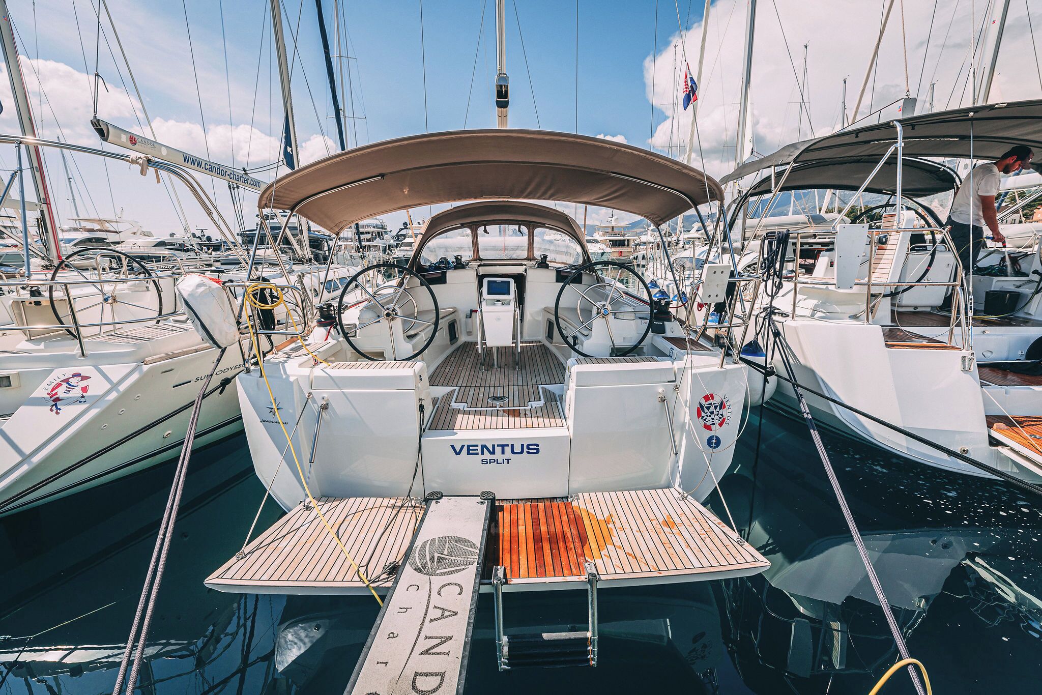 Eine Segelyacht liegt in einer Marina festgemacht, mit einem 'VENTUS SPLIT' Steuerrad, dem Namen 'CANDY' auf dem Deck und der Aufschrift 'CARGO' auf dem Rumpf.