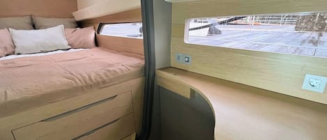 A compact interior with a bed, storage drawers, a window, and a control panel.