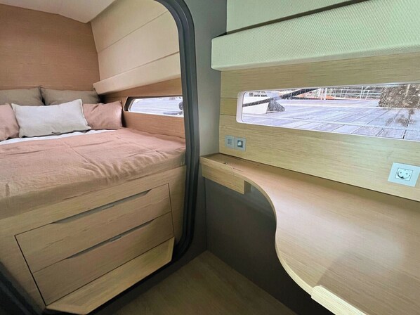 A compact interior with a bed, storage drawers, a window, and a control panel.