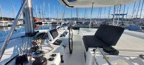 Ein Bootsdeck mit einer Armaturentafel, einem schwarzen gepolsterten Sitz und Blick auf einen Yachthafen mit zahlreichen Booten.