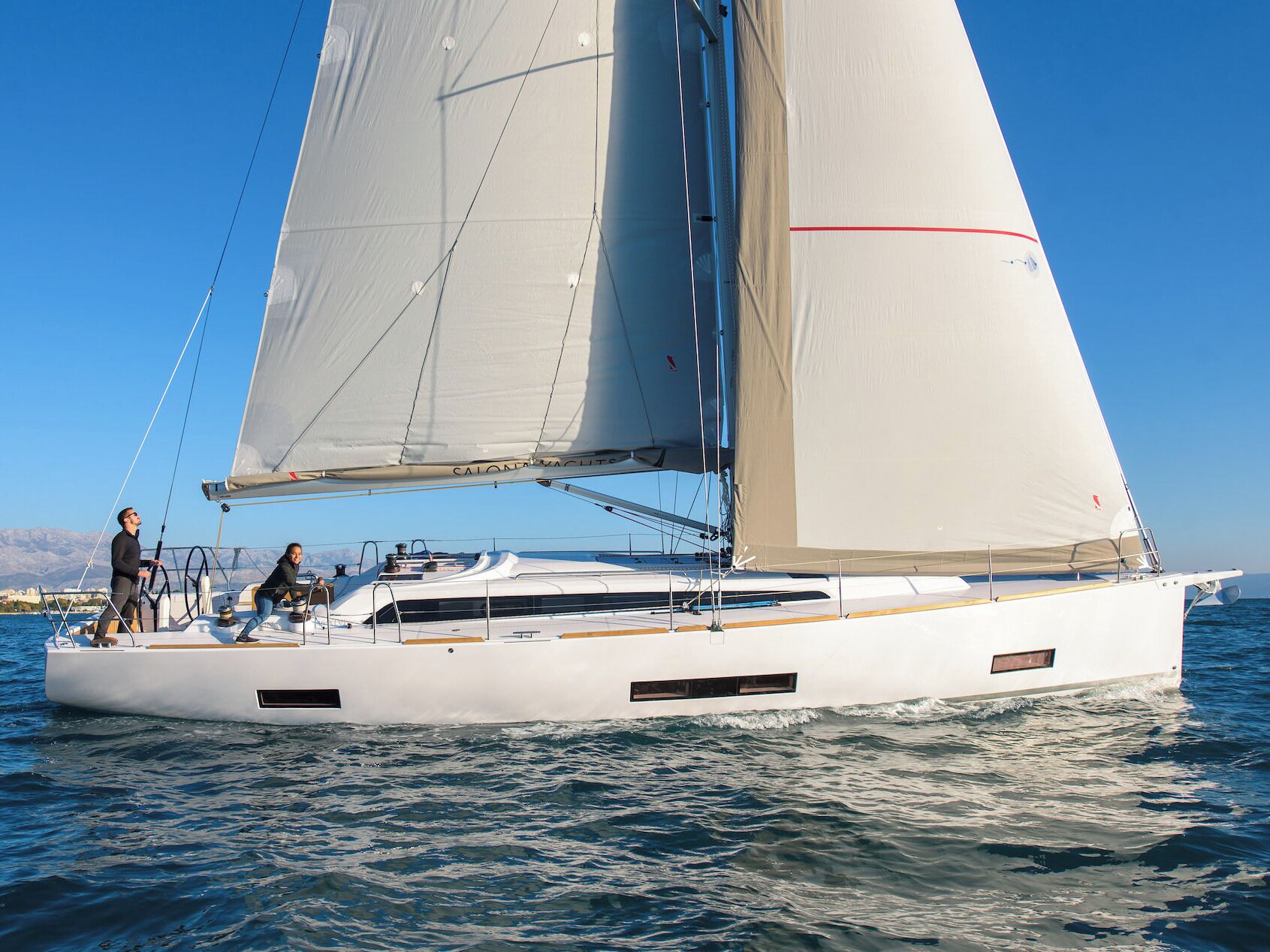 Eine Segelyacht mit weißem Rumpf und zwei Segeln, einem Sitzdeck und einer Person, die am Bug steht.