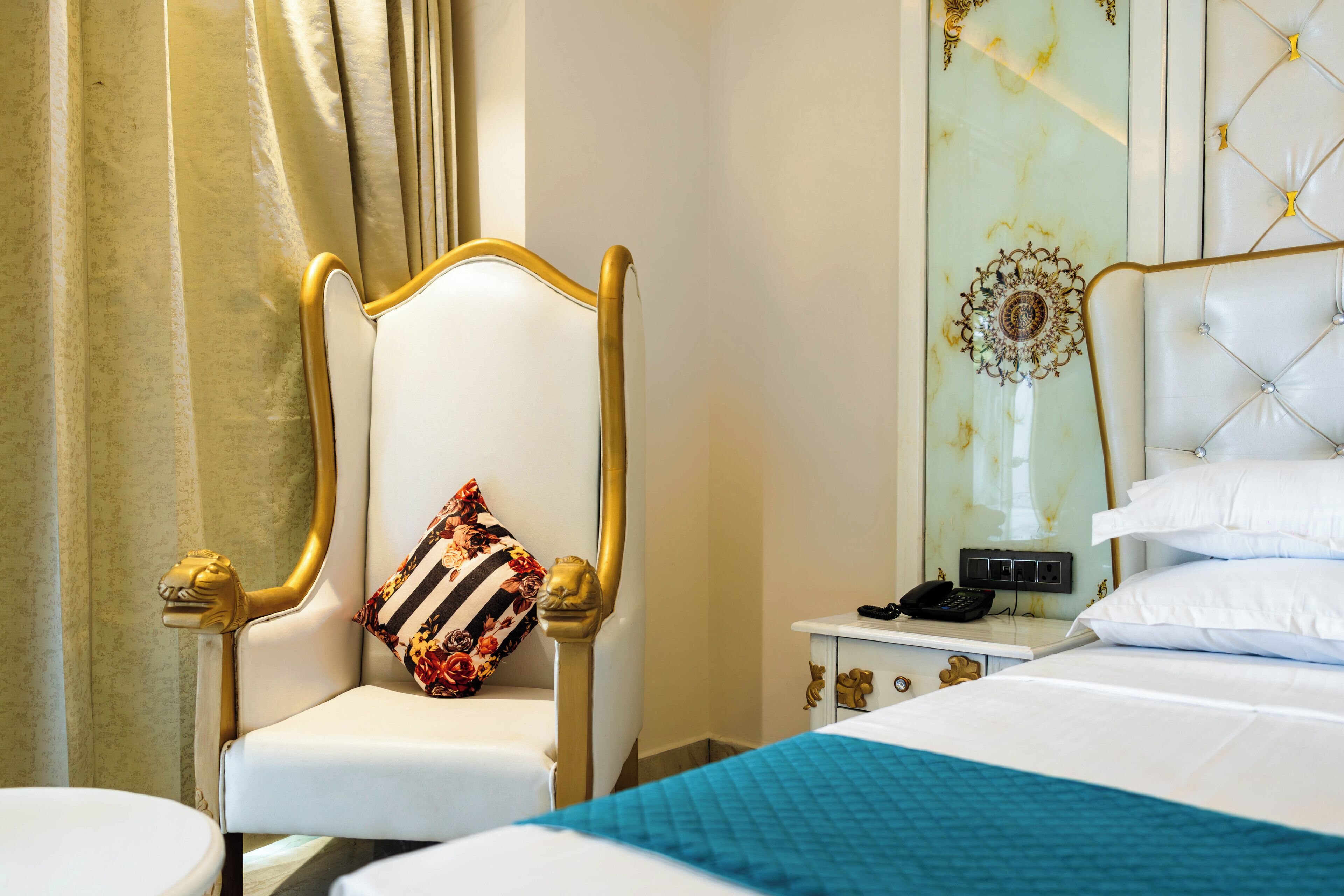 A hotel room with a bed, a chair with a decorative pillow, a bedside table with a phone, and a wall with a decorative panel.