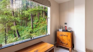 Ein Zimmer mit großem Fenster und Blick auf den Wald, einer hölzernen Bank und einem Schrank mit Gegenständen darauf.