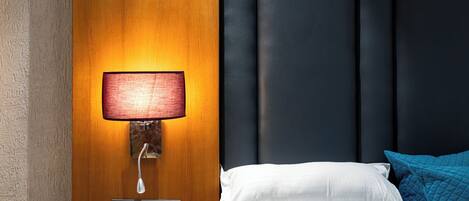 A hotel room with a wooden wall, a wall-mounted lamp, a bed with white and blue pillows, and a dark headboard.