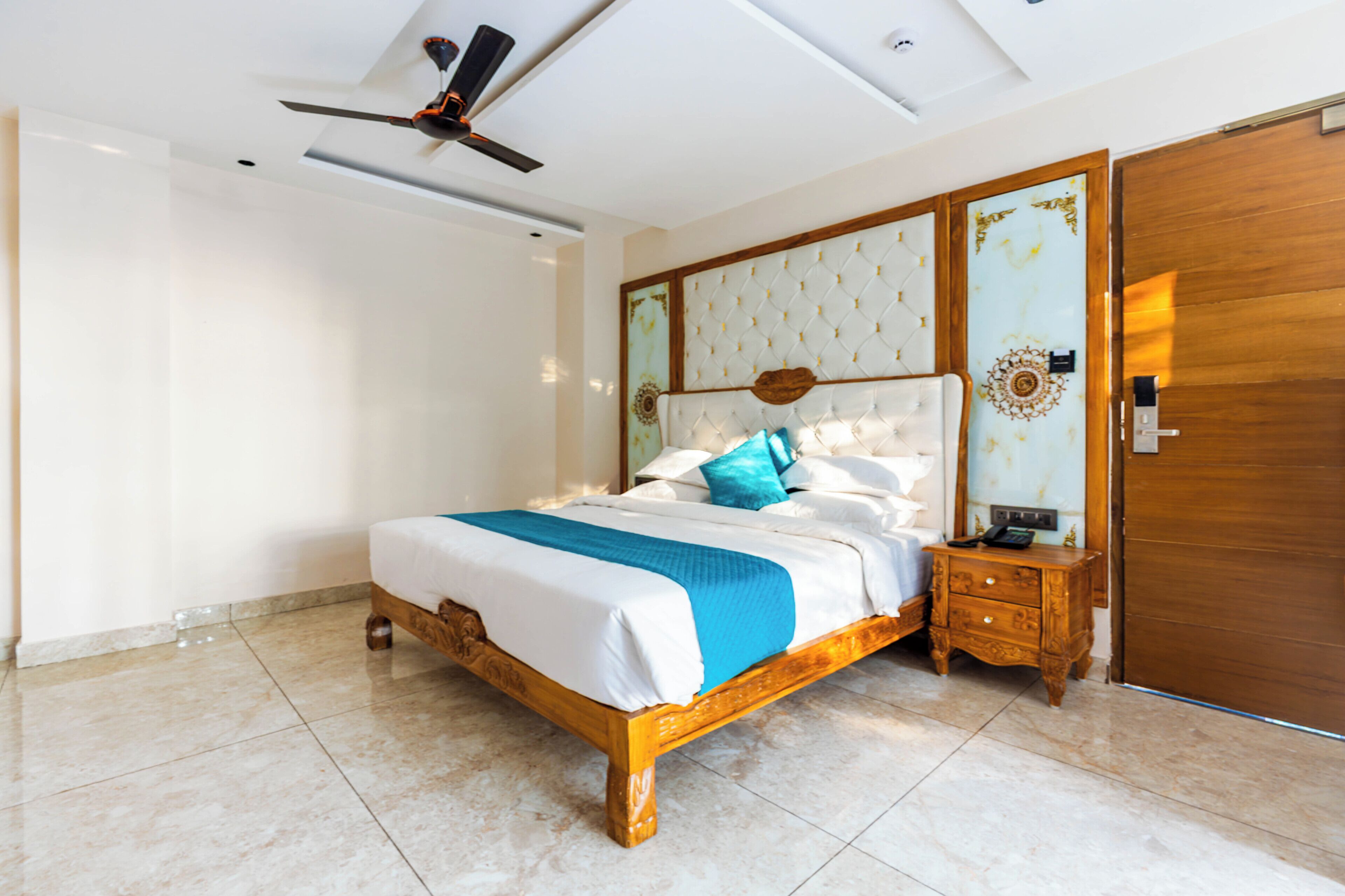 Un dormitorio con una cama, una mesita de noche de madera, un ventilador de techo y una puerta de madera.