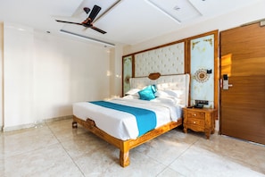 Un dormitorio con una cama, una mesita de noche de madera, un ventilador de techo y una puerta de madera.