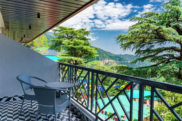 A balcony with a view of a mountainous landscape, a table and chairs, and a patterned floor.