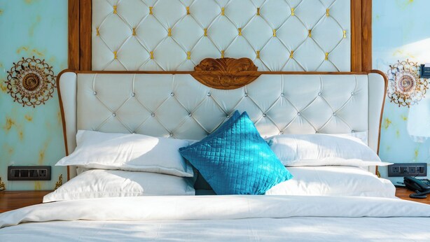 Ein Bett mit einer gesteppten Kopfteil, weißer Bettwäsche und einem blauem Kissen.