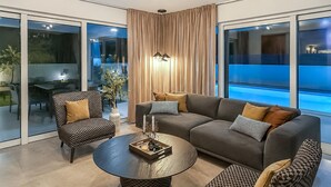 En moderne stue med en grå sofa, mønstrede l ænestole, et rundt sofabord og et stort vindue med gardiner.