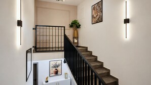 En trappe med sort gelænder, et hvidt konsolbord med en vase og en skulptur, samt et indrammet billede på væggen.