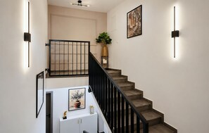 Eine Treppe mit schwarzer Geländer, ein weißer Beistelltisch mit einer Vase und einer Skulptur sowie ein gerahmtes Bild an der Wand.