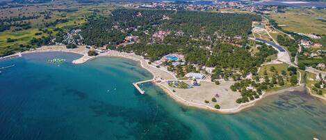An aerial view of a coastal town with a marina, sandy beaches, and a mix of residential and commercial buildings.