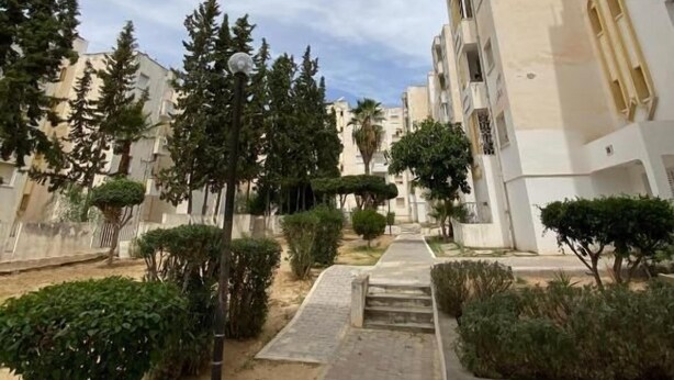 A residential building with a paved pathway, greenery, and a clear sky.