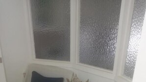 A corner room with two beds, a small table, and a window with frosted glass.