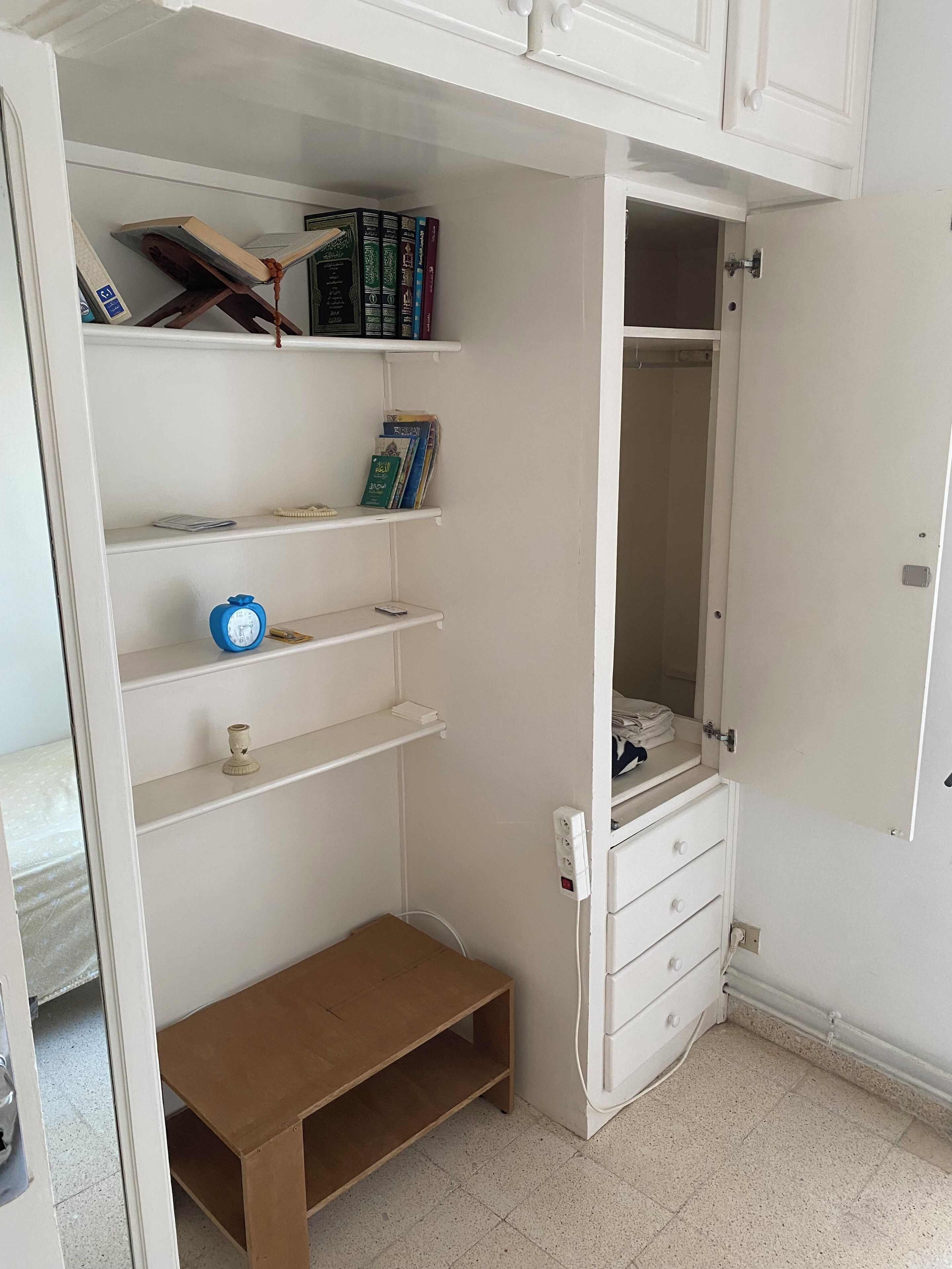 Ein Zimmer mit integriertem Kleiderschrank, Bücherregalen, einem kleinen Tisch und einem Spiegel.