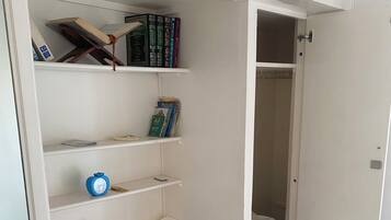 Ein Zimmer mit integriertem Kleiderschrank, Bücherregalen, einem kleinen Tisch und einem Spiegel.