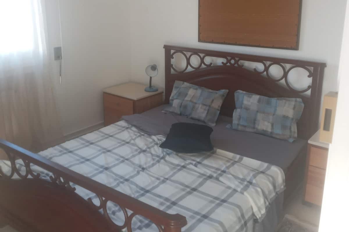 Un dormitorio con una cama de madera, una mesita de noche, una lámpara y una obra de arte colgada en la pared.