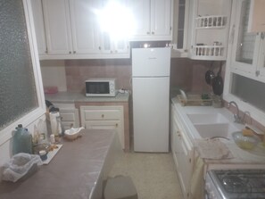 Una cocina compacta con armarios blancos, microondas, refrigerador, pileta y estufa.