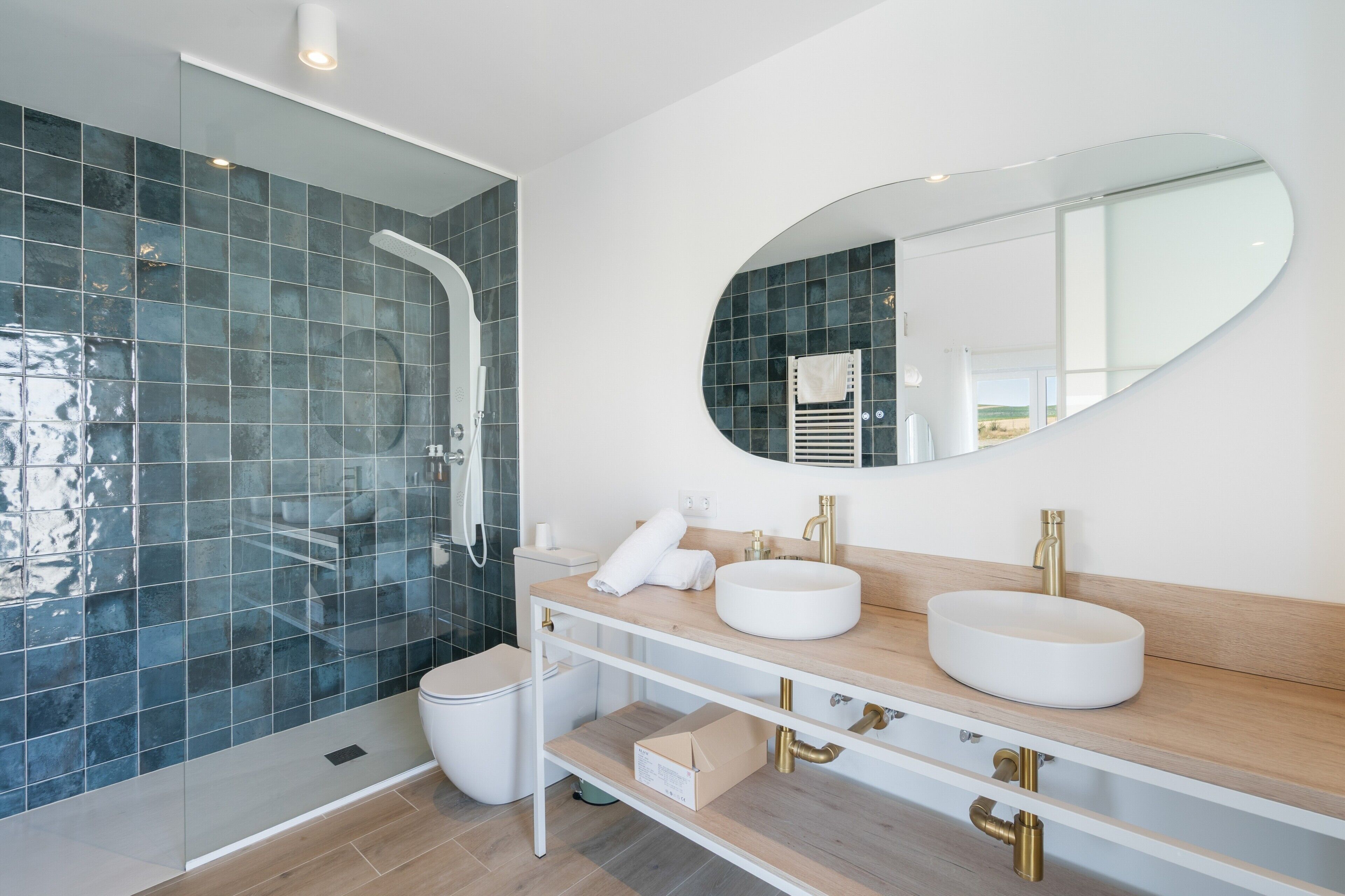 Une salle de bain moderne dotée d’une douche à parois de verre, d’un grand miroir ovale et d’un meuble-lavabo avec deux vasques.