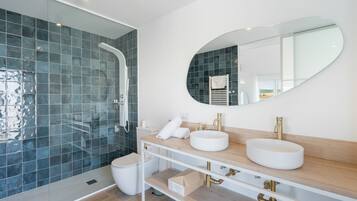 Une salle de bain moderne dotée d’une douche à parois de verre, d’un grand miroir ovale et d’un meuble-lavabo avec deux vasques.