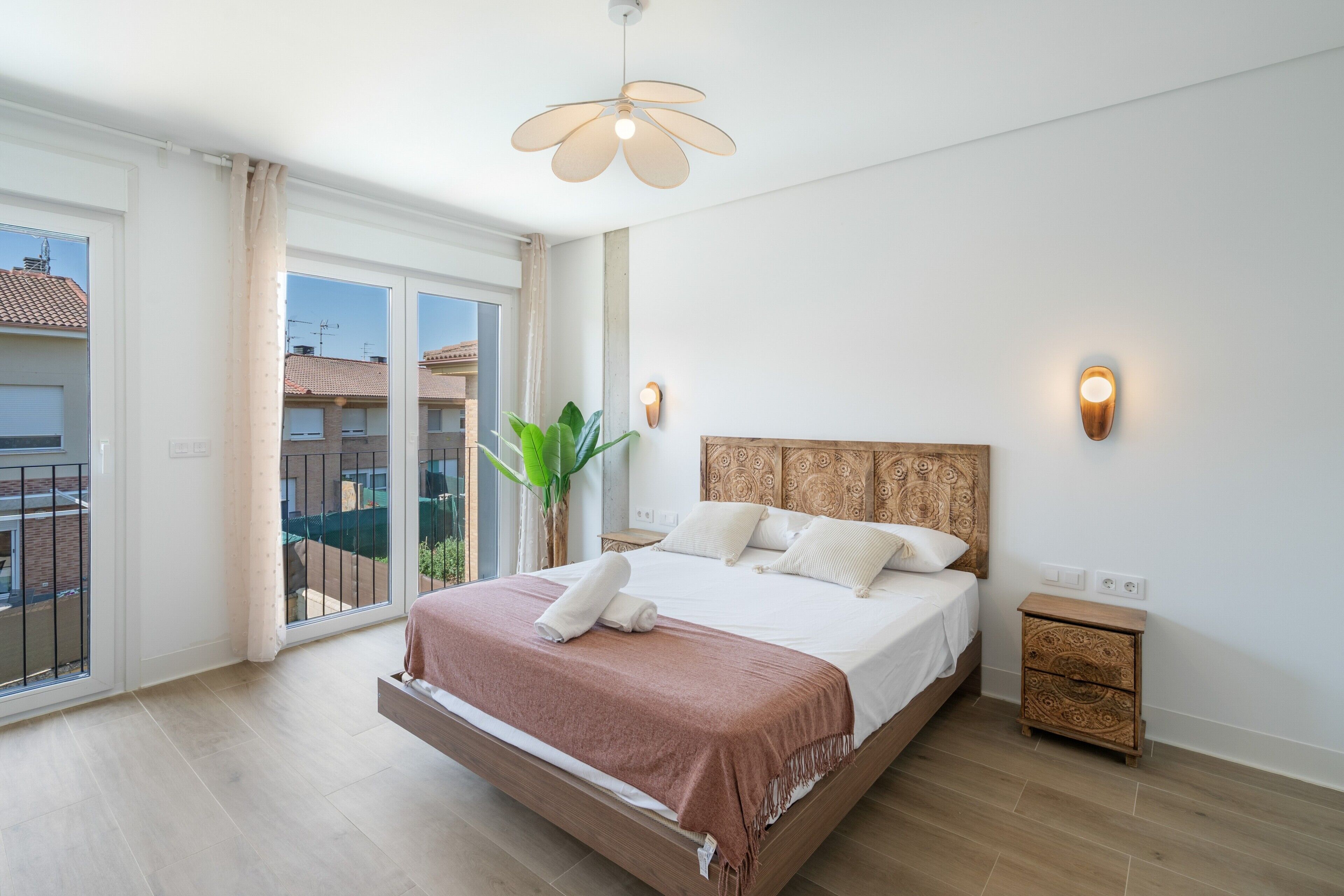 Ein Schlafzimmer mit einem großen Bett, einem Holzkopfende, einem Nachttisch, einer Wandleuchte und Blick nach draußen durch eine Schiebetür.