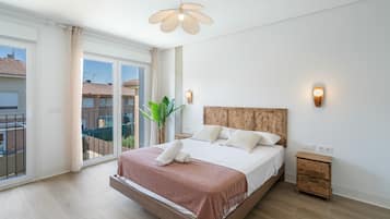 Ein Schlafzimmer mit einem großen Bett, einem Holzkopfende, einem Nachttisch, einer Wandleuchte und Blick nach draußen durch eine Schiebetür.