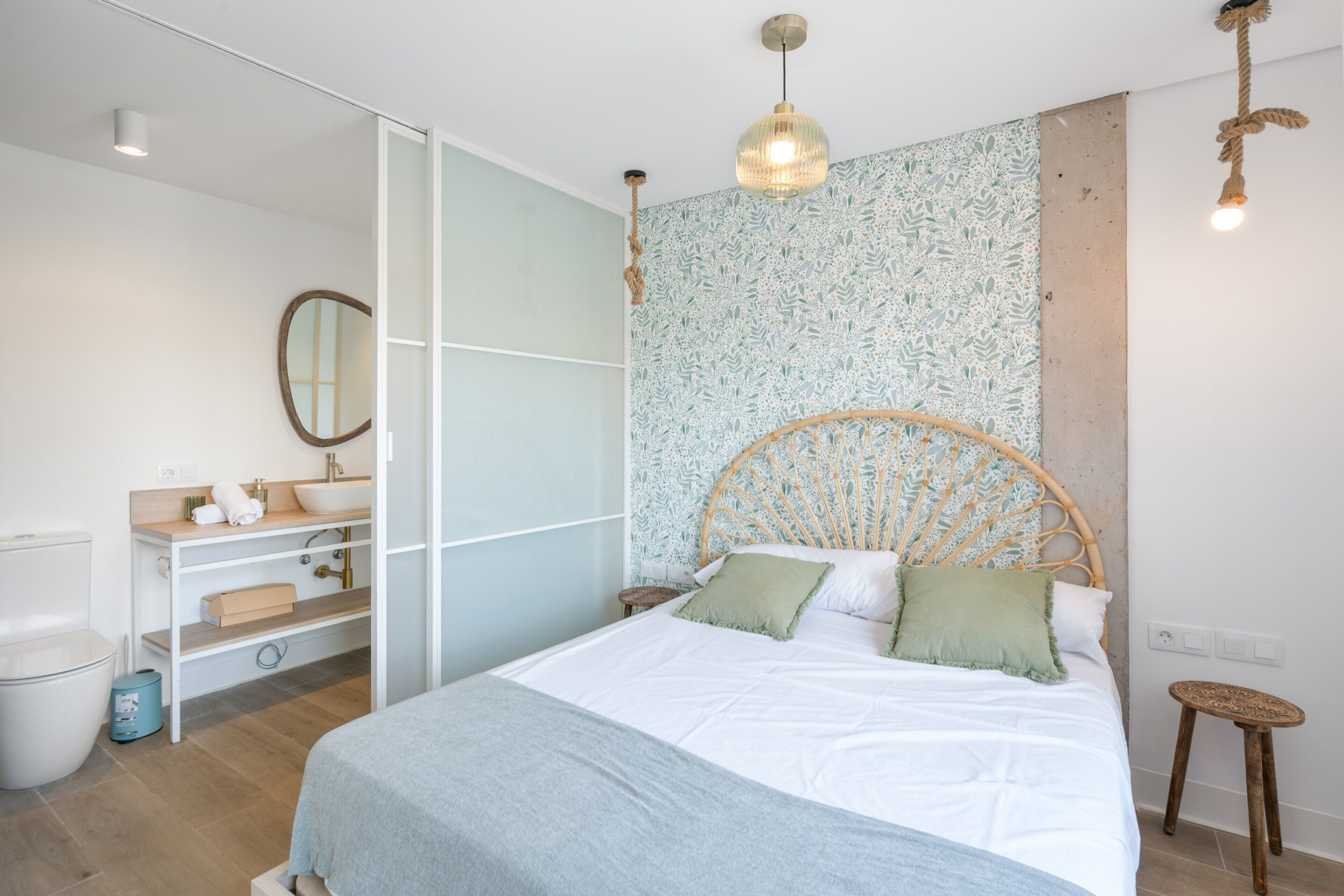 Quarto com cama, mesas de cabeceira, um espelho e luminária pendente.