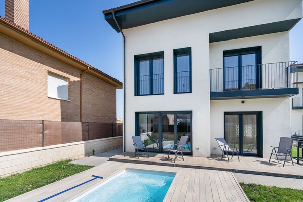 A modern two-story building with a swimming pool, outdoor seating, and a fenced backyard.