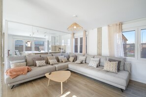 A modern living room with a sectional sofa, a round coffee table, and a large mirror reflecting the room.