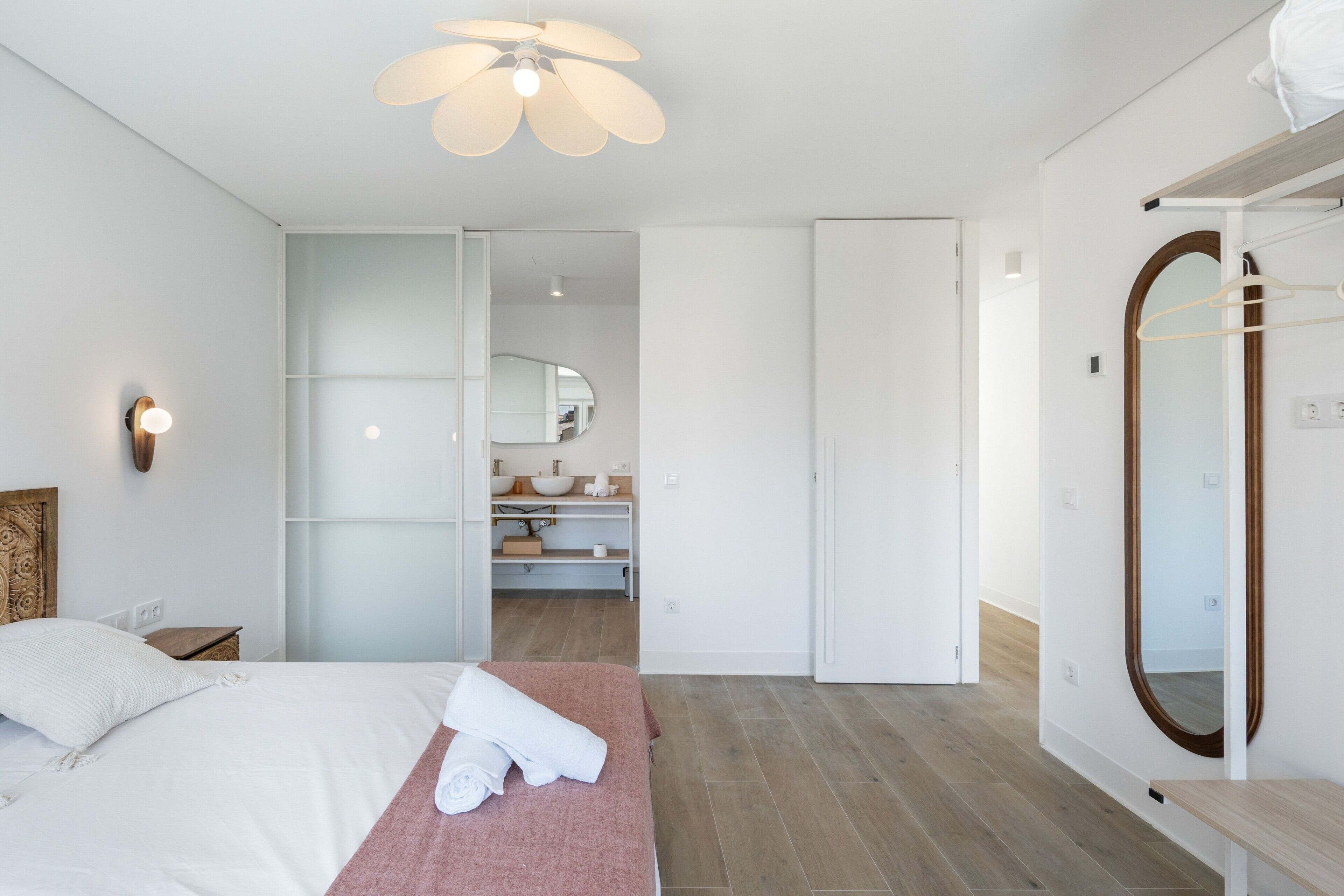 Ein modernes Schlafzimmer mit Bett, Nachttisch, großem Spiegel und Deckenventilator.