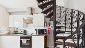 A modern kitchen with white cabinets, a built-in oven, a microwave, and a wooden countertop. - The Mews - 1 Bed Holiday Home - Langland (Swansea)