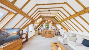 Ein geräumiges Dachzimmer mit Holzbalkendecke, einem Fernseher, einem Sofa, einem Couchtisch und einer Küchenzeile.