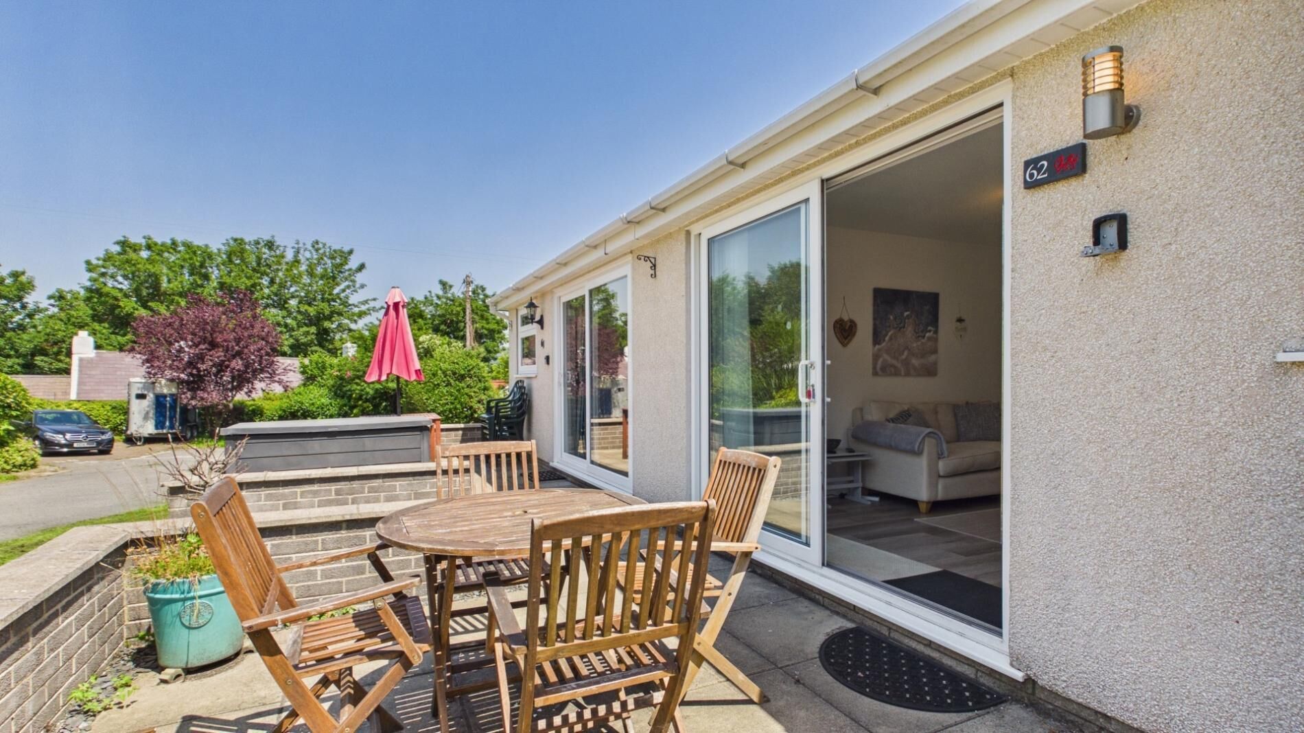 A patio with wooden furniture, a red umbrella, and a sliding glass door leading to an interior space with a sofa and a coffee table.