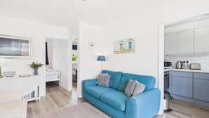 Ein modernes Wohnzimmer mit einem blauen Sofa, einem Essbereich und einer Küche mit weißen Schränken.
