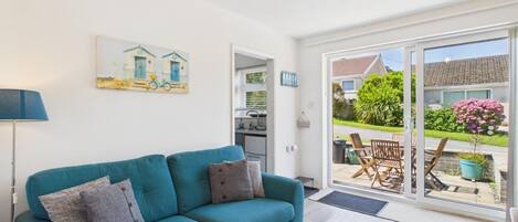 A teal sofa with cushions, a painting of houses, and a view of a garden through a sliding glass door.