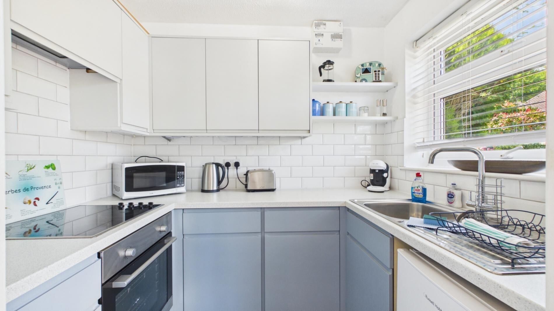A modern kitchen with white cabinets, a microwave, toaster, kettle, coffee maker, and a dish rack.