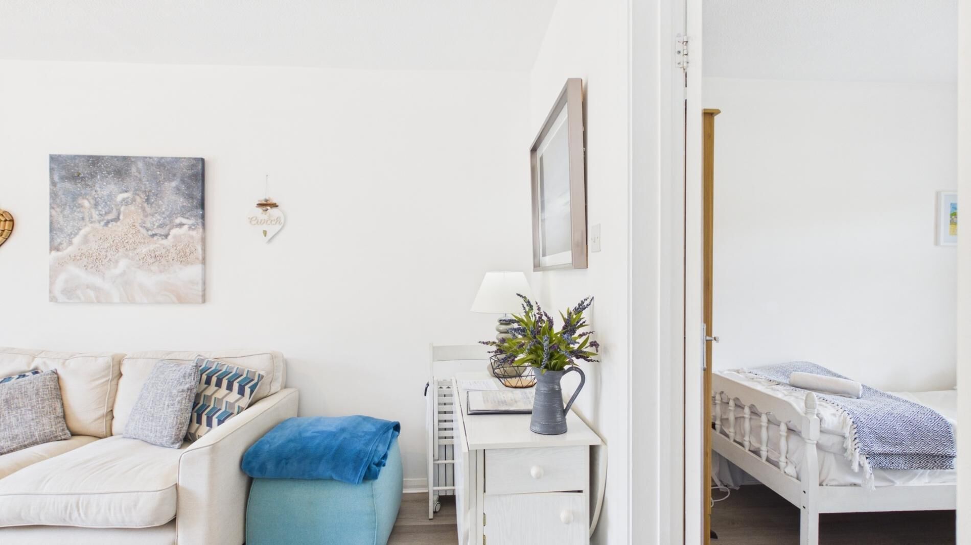 A bedroom with a bed, a desk with a lamp, a chair, and a small table with a plant.