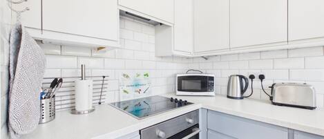 A modern kitchen with white cabinets, a microwave, a kettle, a toaster, and a gas stove.