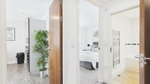 A modern hotel room with a bed, a bathroom with a bathtub, and a hallway with a plant. - 40 Meridian Tower - 1 Bedroom Apartment - Swansea (Swansea)