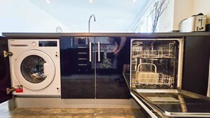 Cocina compacta con lavadora, lavavajillas y una persona al fondo.