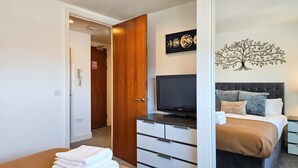 Un dormitorio con cama, televisor, cómoda y una obra de arte en la pared.