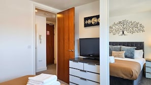 Quarto com cama, televisão, penteadeira e uma obra de arte na parede.