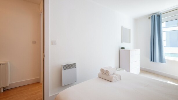 Une chambre à coucher avec un lit, un radiateur, une armoire et une fenêtre avec des rideaux.