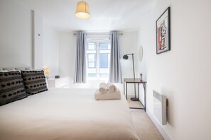 Ein Schlafzimmer mit einem großen Bett, einem Nachttisch mit Lampe, einem Fenster mit Vorhängen und einer Heizung.