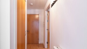 Un couloir avec des portes en bois, un radiateur blanc et un interrupteur sur le mur.